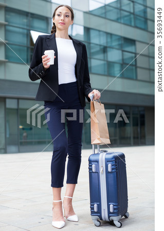 Adult businesswoman in suit with suitcase is drinking coffee Adult businesswoman in suit with suitcase is drinking coffee 35693449
