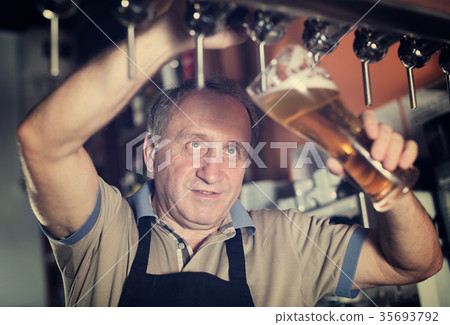 Smiling barman is pouring unbottled beer for next client Smiling barman is pouring unbottled beer for next client 35693792