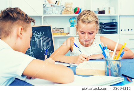 Boy with girl are writing in notebook their homework Boy with girl are writing in notebook their homework 35694315