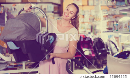 Pregnant woman carefully choosing infant car seat in kids mall Pregnant woman carefully choosing infant car seat in kids mall 35694335