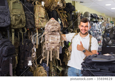 guy looking camouflage backpack in army store guy looking camouflage backpack in army store 35694619