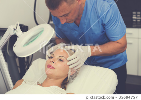 Man doctor is analysing skin on face of female patient before the procedure 35694757