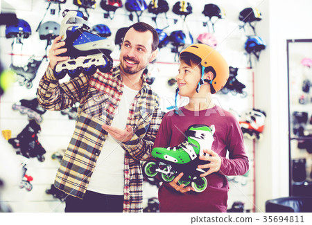 Seller assisting boy in choosing roller-skates Seller assisting boy in choosing roller-skates 35694811
