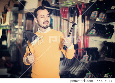 Man choosing various tools in garden equipment shop Man choosing various tools in garden equipment shop 35695045