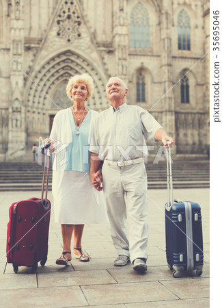 Mature travelers strolling with luggage Mature travelers strolling with luggage 35695046