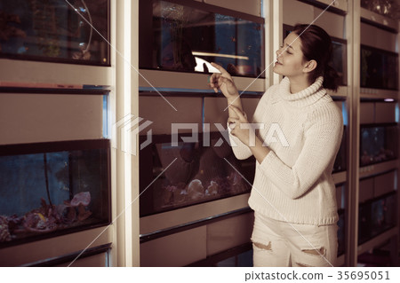 Girl in aquarium shop points to colored fish Girl in aquarium shop points to colored fish 35695051