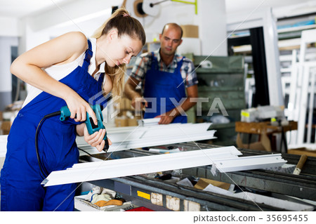 Workwoman drilling PVC window profiles in workshop 35695455