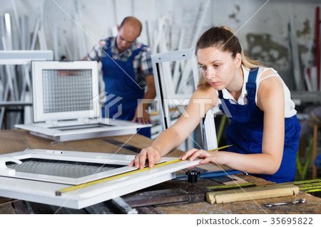 Female worker measuring finished metal-plastic window in workshop Female worker measuring finished metal-plastic window in workshop 35695822