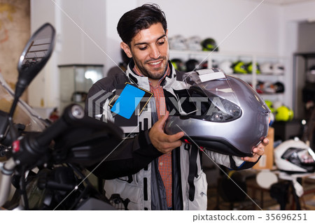 Man in moto jacket is choosing new helmet for motorbike in the store. 35696251
