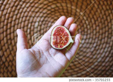 Fresh sweet ripe fig in hand on wicker place mat Fresh sweet ripe fig in hand on wicker place mat 35701255