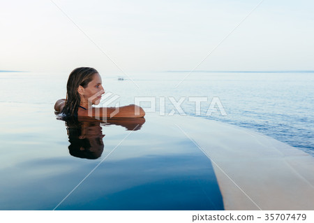 Woman at infinity swimming pool with sea view 35707479