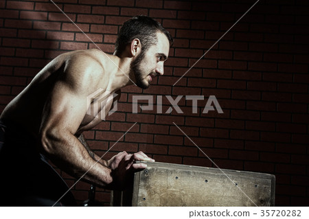 Muscular man pushes a wooden box 35720282