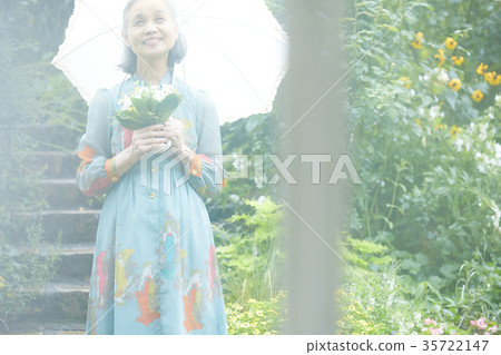 Senior woman holding a parasol in the garden Senior woman holding a parasol in the garden 35722147