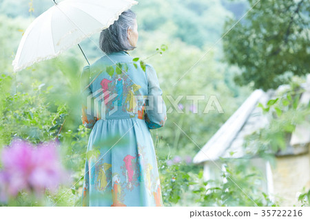 拿著遮陽傘的資深婦女在庭院裡 拿著遮陽傘的資深婦女在庭院裡 35722216