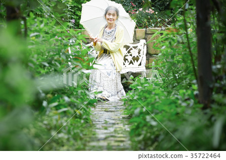 Senior woman holding a parasol in the garden Senior woman holding a parasol in the garden 35722464