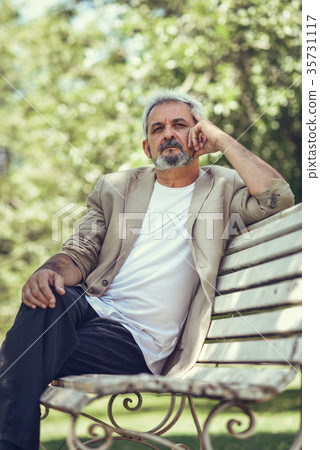 Pensive mature man sitting on bench in an urban park. Pensive mature man sitting on bench in an urban park. 35731117