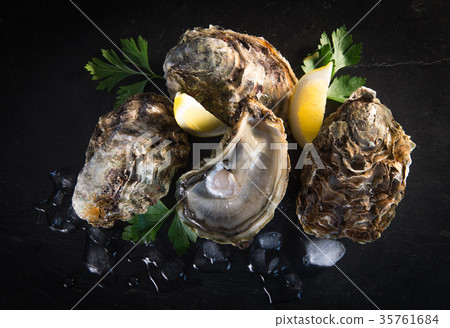 Opened oysters on stone slate plate with lemon and oyster knife 35761684