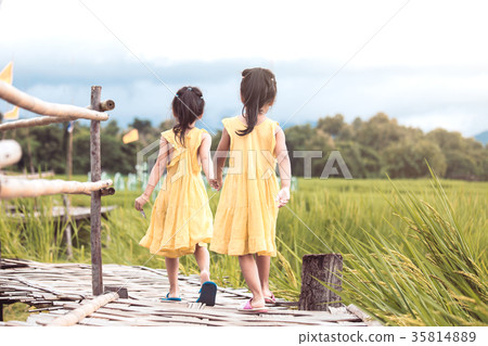 two little girls holding hand and walking together 35814889