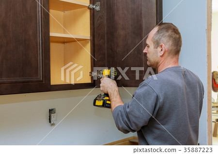 Handyman fixing kitchen's cabinet with screwdriver 35887223
