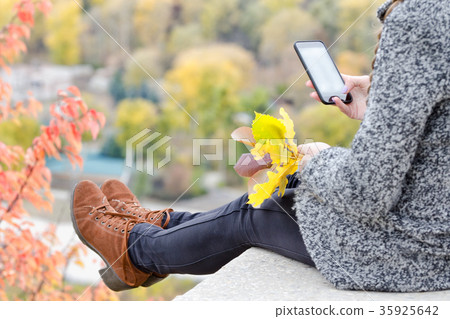 Girl with a phone sits on a hill, yellow leaves Girl with a phone sits on a hill, yellow leaves 35925642