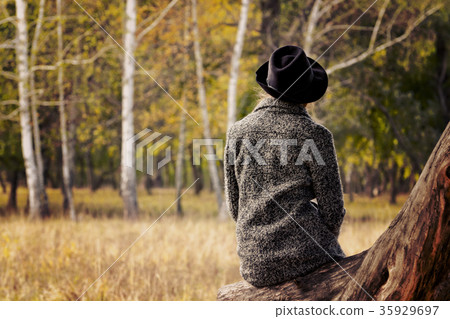 Girl in a hat sitting on a log in autumn forest Girl in a hat sitting on a log in autumn forest 35929697