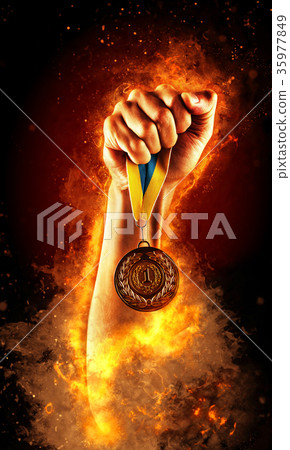 Man's hand in a fire is holding up gold medal 35977849