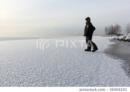 Man walking on  ice of a freezing pond at sunset 36008202