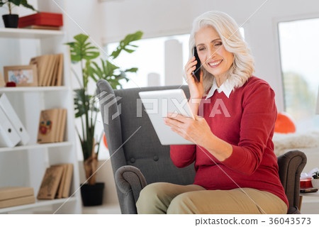 Beaming retired woman talking on phone and using Beaming retired woman talking on phone and using 36043573