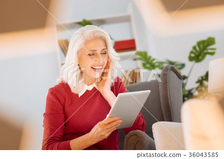 Radiant elderly woman laughing while using tablet 36043585