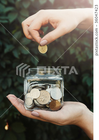 Hand putting coins in glass jar, green background 36047423