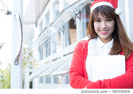woman wear santa hat holding laptop at her shop. asian female wear white shirt and red knitting cardigan with computer at home. christmas holiday portrait. 36049069