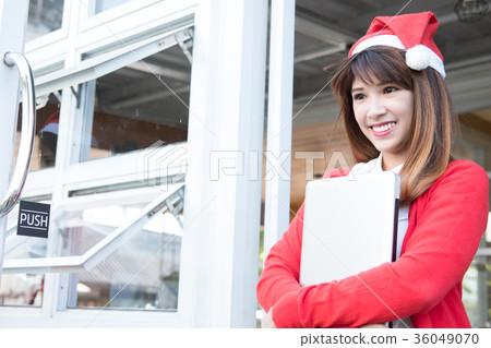 woman wear santa hat holding laptop at her shop. asian female wear white shirt and red knitting cardigan with computer at home. christmas holiday portrait. woman wear santa hat holding laptop at her shop. asian female wear white shirt and red knitting cardigan with computer at home. christmas holiday portrait. 36049070