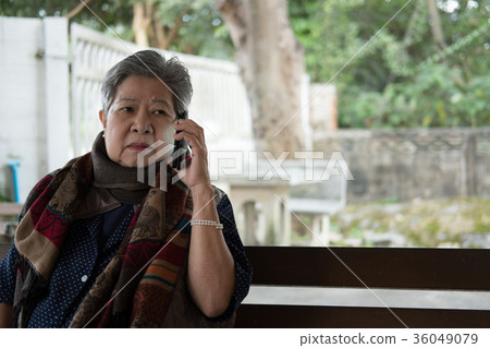elder woman talk on mobile phone while sitting on bench in garden. elderly female speaking on smartphone in park. senior have phone conversation elder woman talk on mobile phone while sitting on bench in garden. elderly female speaking on smartphone in park. senior have phone conversation 36049079