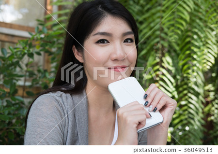 asian woman sit at outdoor cafe. young female adult with natural make-up hold mobile phone at coffee shop. attractive teenager smile with happiness in garden asian woman sit at outdoor cafe. young female adult with natural make-up hold mobile phone at coffee shop. attractive teenager smile with happiness in garden 36049513