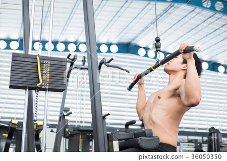 young man execute exercise with weightlifting machine in fitness center. male athlete pump up muscle with pull down machine in gym. sporty guy working out in health club. 36050350