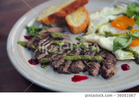 Grilled beef steak with toast , fried egg and vegetables on top with pesto sauce 36081067