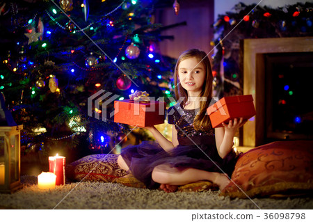 Happy girl opening Christmas gifts by a fireplace 36098798