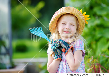 Adorable little girl wearing straw hat and childrens garden gloves playing with her toy garden tools 36106346