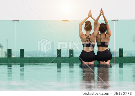 Two attractive women are playing yoga. At the pool for her good 36120778