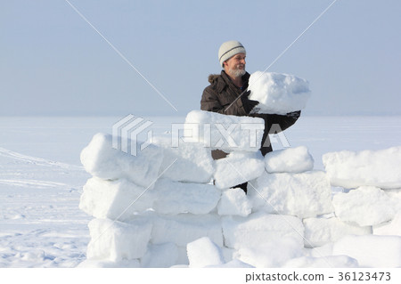 Man with a beard in a gray cap building an igloo  36123473