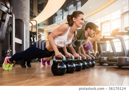 Three young people doing the kettlebell plank Three young people doing the kettlebell plank 36170124