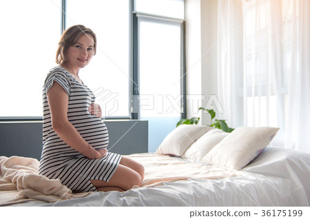 Happy pregnant woman sitting on bed with joy 36175199