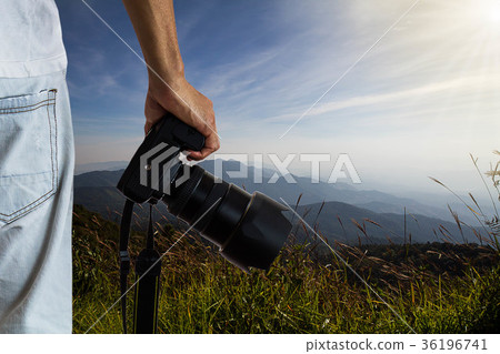 Man holding dslr digital camera on blurred nature Man holding dslr digital camera on blurred nature 36196741