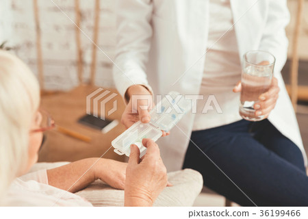 Young nurse consulting aged patient at home 36199466