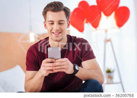 Cheerful young man smiling while writing message Cheerful young man smiling while writing message 36200768