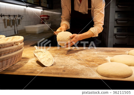 baker portioning dough with bench cutter at bakery 36211505