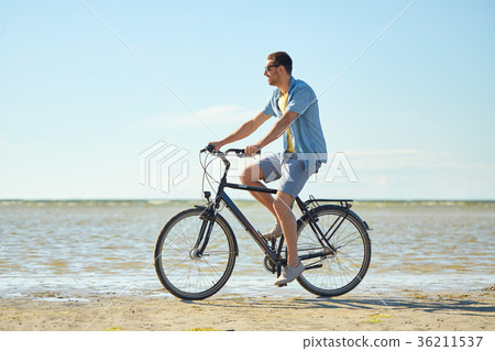 happy man riding bicycle along summer beach 36211537