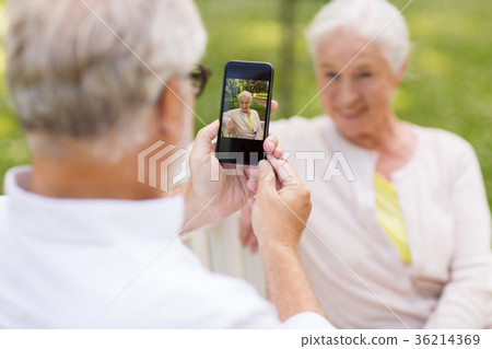 old woman photographing man by smartphone in park 36214369