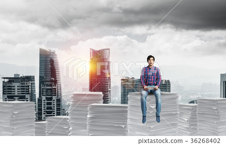 Attractive man sitting on pile of paper documents. 36268402