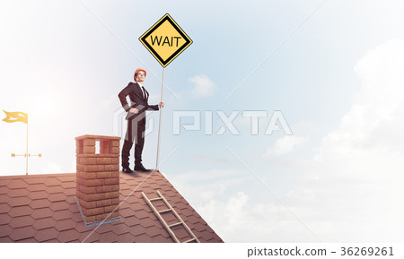 Young businessman on house brick roof holding yellow signboard. 36269261